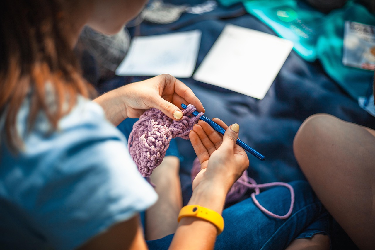 knitting-4639828_1280 Frau häkelt mit dicker lila Wolle und blauer Häkelnadel.